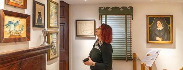 A woman standing in a house museum looking at paintings on a wall