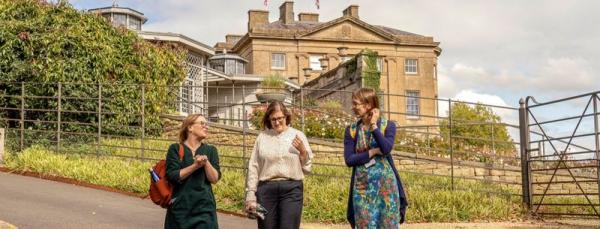 Three women walking along a path in front of a classical style museum
