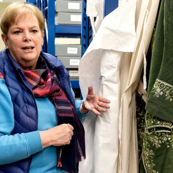 A woman takes a historical green coat out of a hanging calico bag