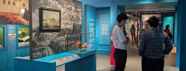 A group of people talking in a blue gallery with shoes on display.