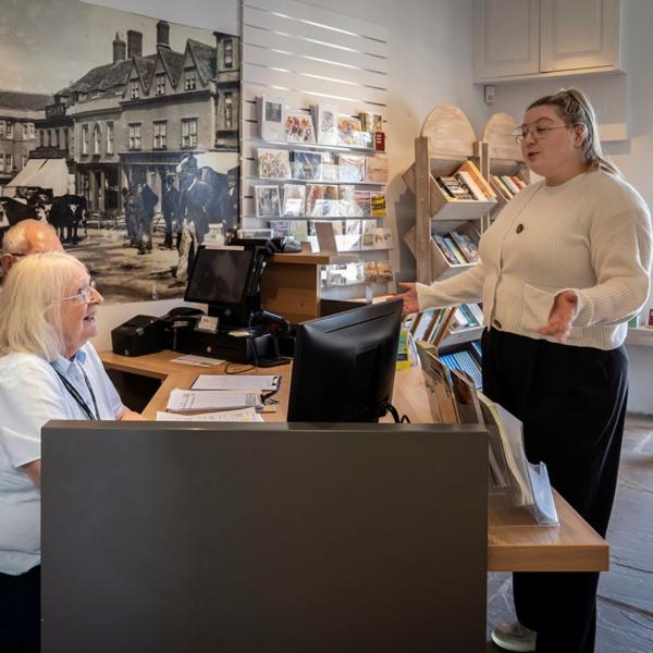 A woman talking to two people behind a desk in a museum reception