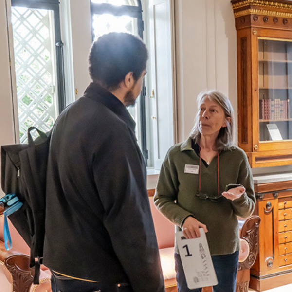 A woman talking to a man in a museum, she is wearing a badge and glasses on a chain around her neck