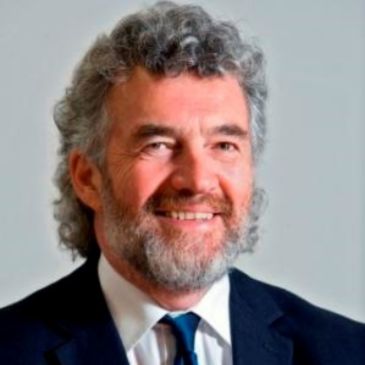 A man with grey hair and a beard (eddie kane) is smiling at the camera