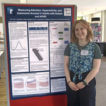 A person (Eve Park) stands behind a poster, smiling