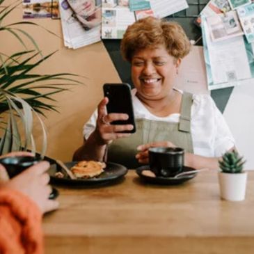 A person is sitting at a table smiling and looking at a mobile phone