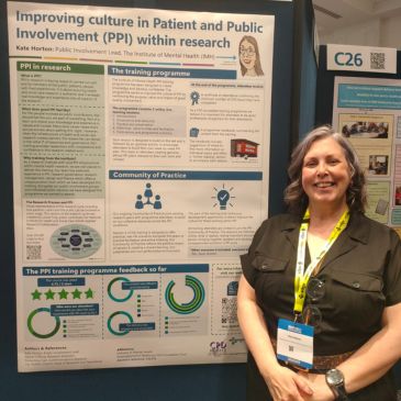 A person (Kate Horton) is smiling and standing beside a poster