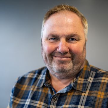 A person (Mike Slade) is wearing a checked shirt and smiling at the camera