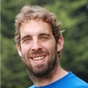 A headshot of a person with facial hair smiling at the camera