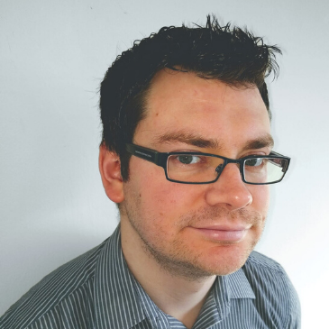 A person wearing spectacles is smiling at the camera