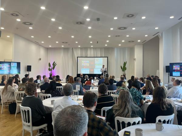People are sat around tables facing a person giving a presentation
