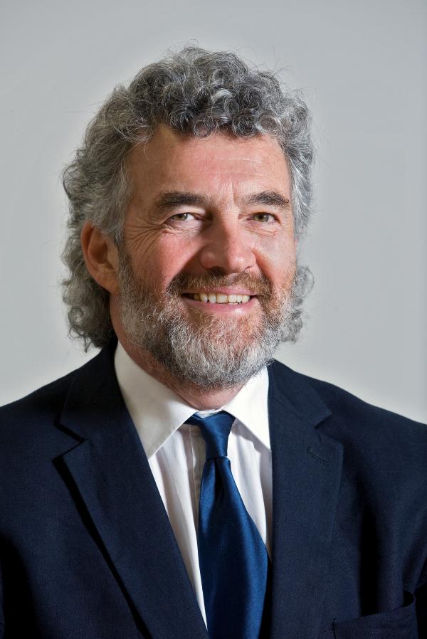 A person wearing a dark suit and tie is smiling at the camera