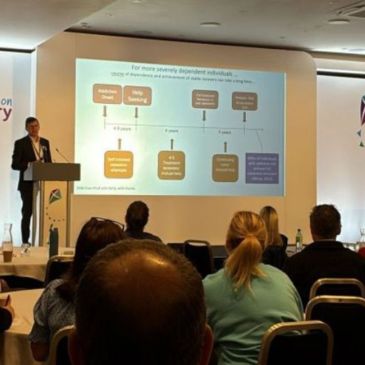 A person stands at a lectern delivering a presentation 