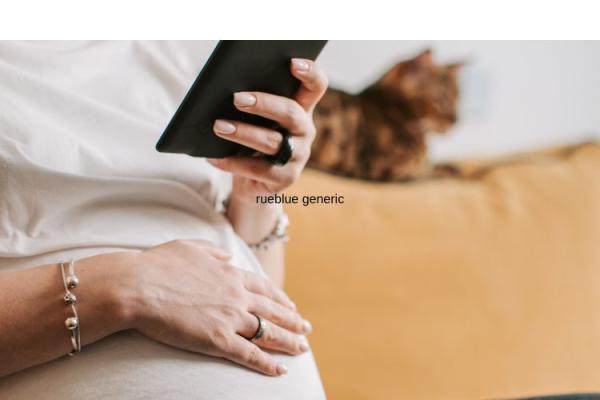 A pregnant person rests one hand on their stomach whilst holding their phone in the other hand. A cat reclines in the background