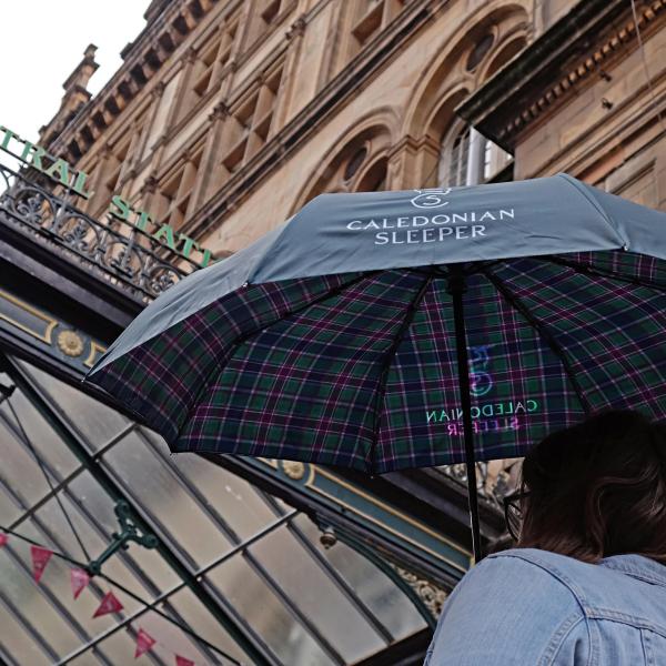 Woman holding Caledonian Sleeper compact tartan umbrella