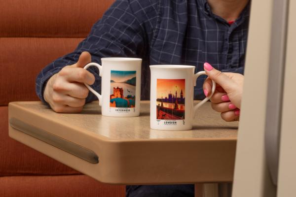 Man and woman using Caledonian Sleeper destination mugs in Club Car