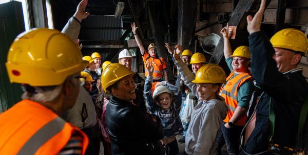 Visitors in hard hats holding their hands up as part of an activity on a tour at the NCMM