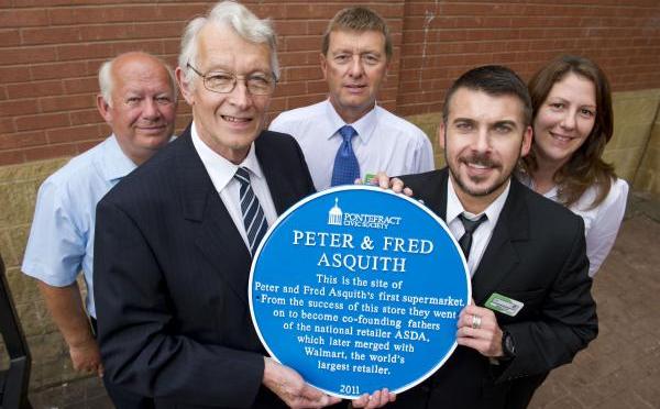 Five people in a group photo, the two people in the front are holding a blue plaque