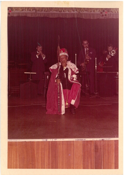 Charlie Williams footballer, on stage dressed in royal regalia with a spear. At the party to celebrate his MBE. Image courtesy of Barnsley Museums and Archives