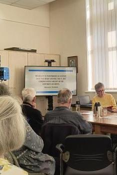 A group of people gathered on seats around a table for a talk led by Gill Crawshaw