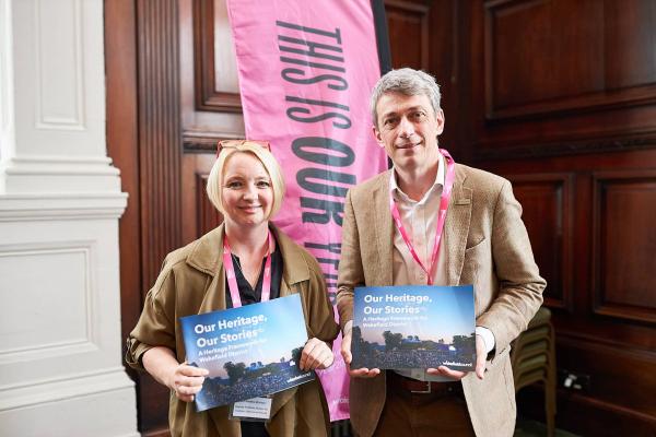 Two people holding copies of the Wakefield District Heritage Framework booklet and smiling to the camera