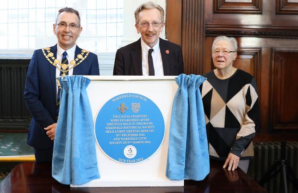 Three people stood behind a blue plaque display with curtains either side for unveiling