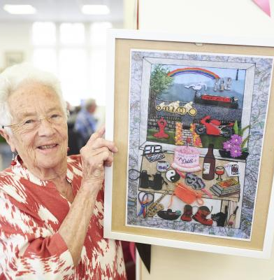 A person holding up a framed textile artwork depicting objects and memories relating to Horbury.