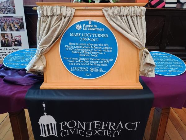 Blue plaque for Mary Lucy Turner on a board with curtains either side