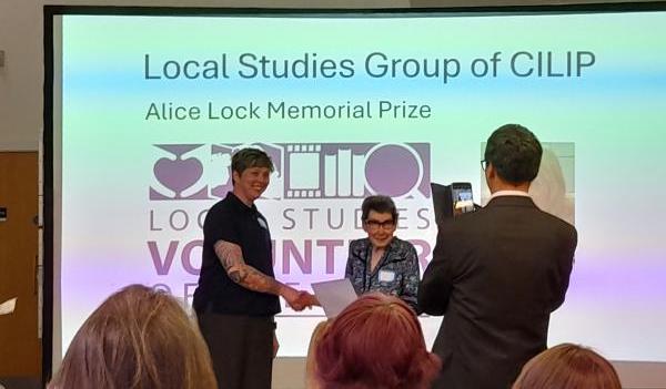 A person receiving an award in front of a projector screen