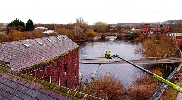 Two workers on a cherry picker next to Queen's Mill