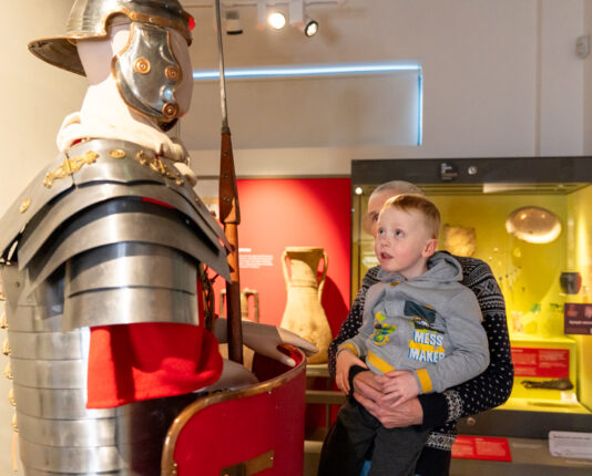 A young children is held up by their parent to see Roman armour in a museum