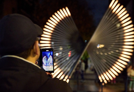 Light installation Sentinel on display at night with a person taking a photo of it