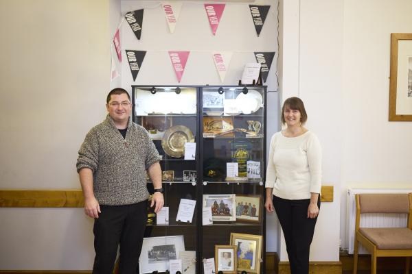 Two people stood in front of a display cabinet filled with historic objects and archival material.