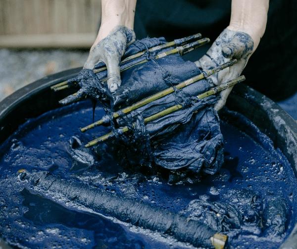 A pair of hands holding fabric in a dark blue dye