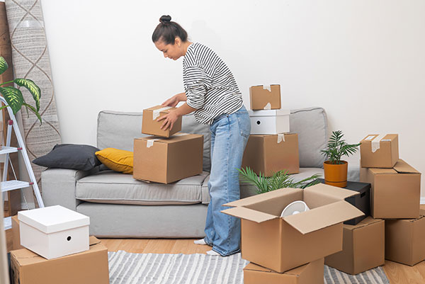 A woman stood by a sofa packing cardboard boxes