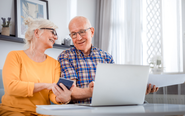 elderly couple sat in front of laptop talking to each other