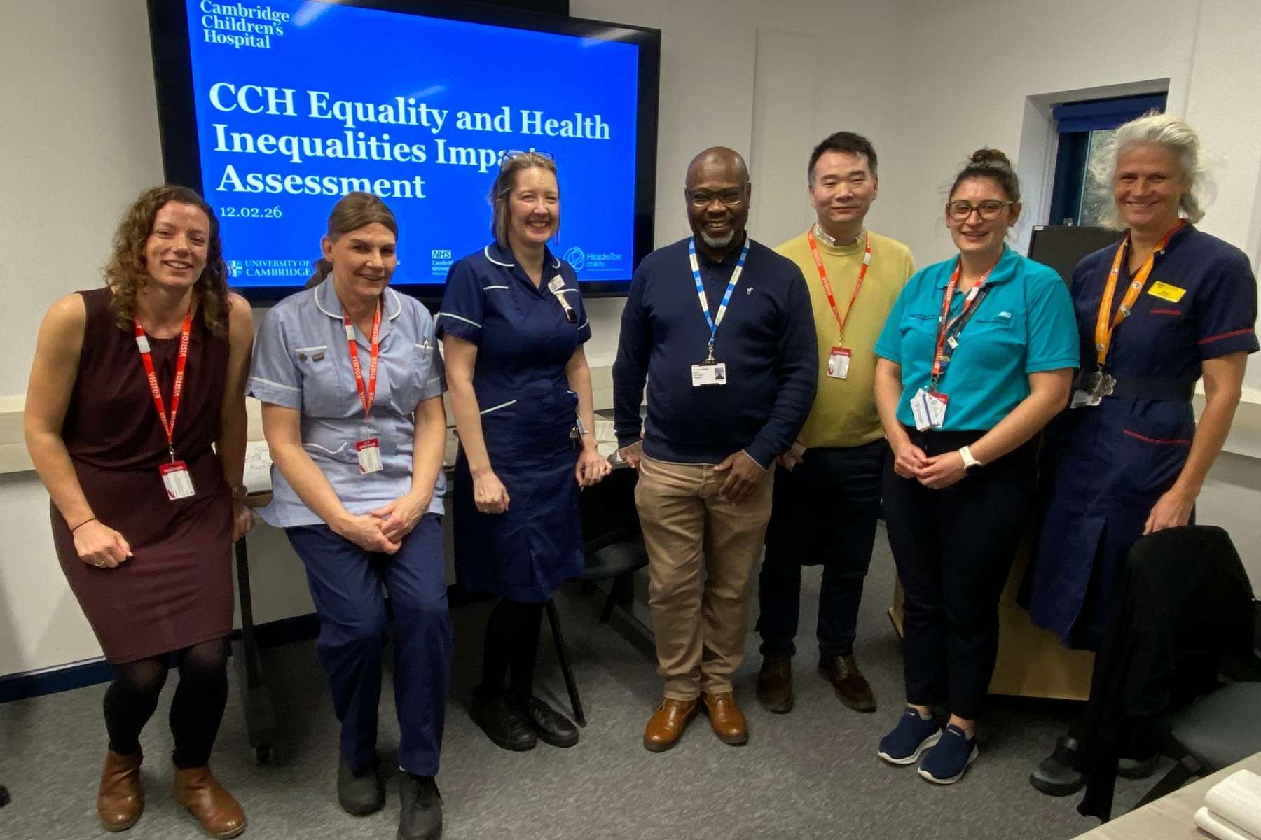 A group of people standing together in a room. some are in nurses uniform. Behind is a screen saying CCH Equality and Health Inequalities Impact Assessment.