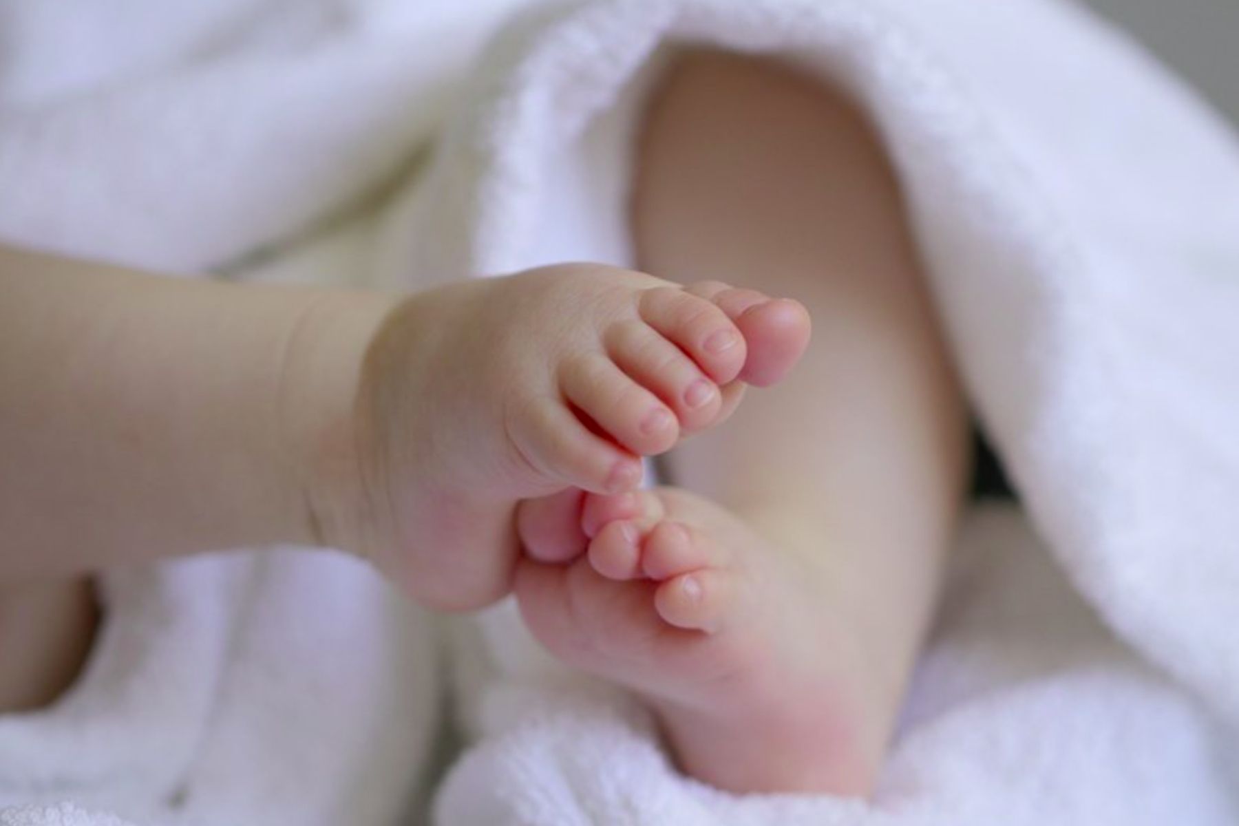 A photo of a baby's feet with a snuggly white blanket wrapped around the legs