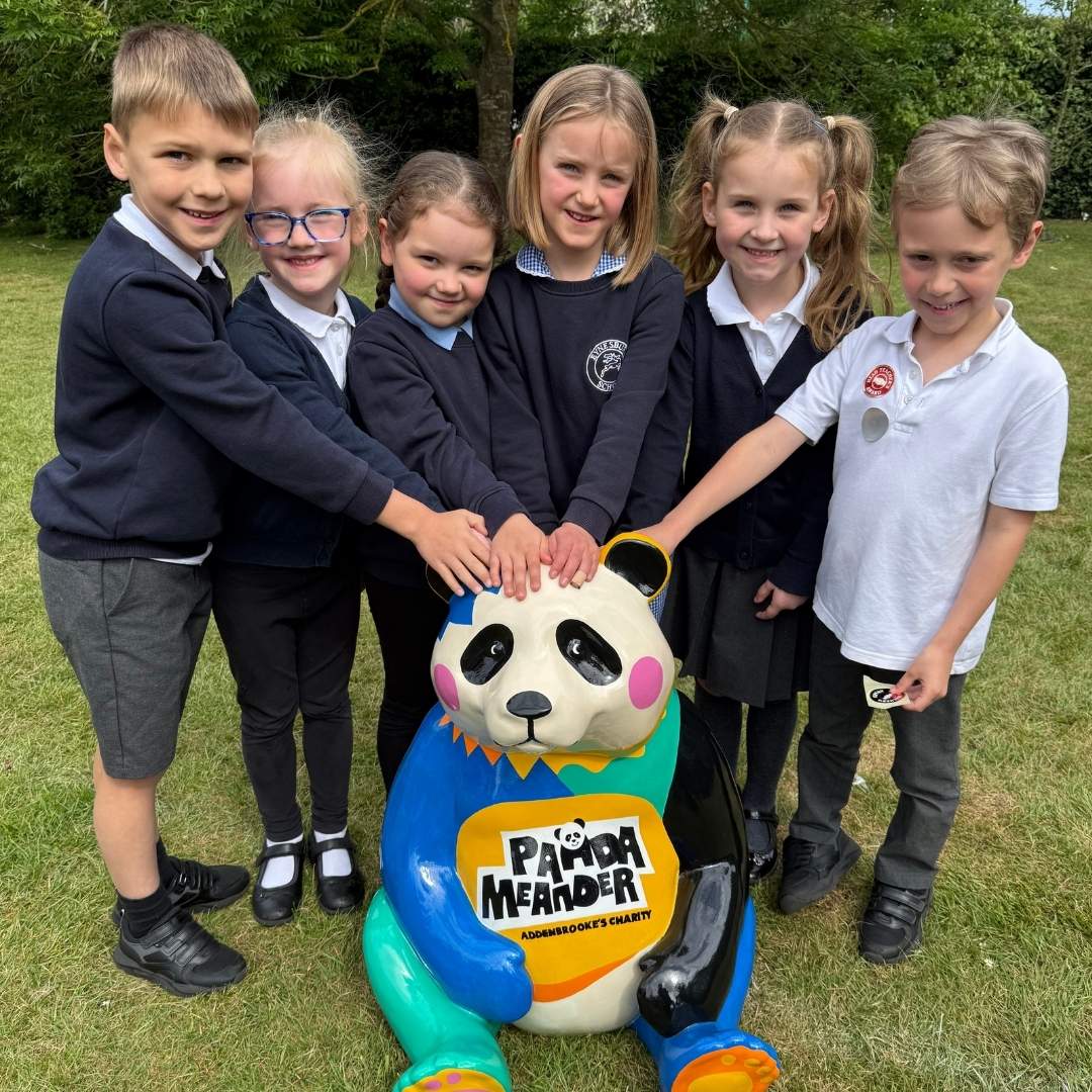 Six primary school children with a sculpture of a panda cub for the Panda Meander fundraising trail. They are touching his head and smiling