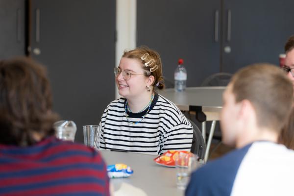 a young woman with a stripey t shirt and her hair pinned up by clips, sitting around a table with other young people