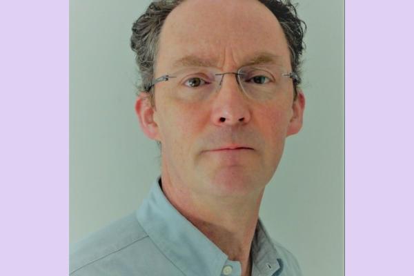 A headshot of a man with receding brown hair, glasses and a pale blue shirt