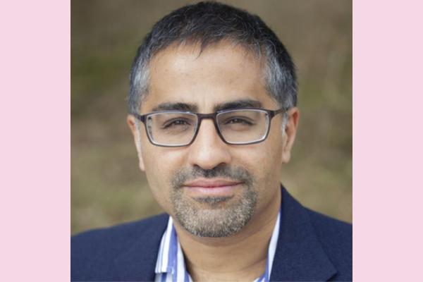 A headshot of a man with greying hair, a greying goatee bear, glasses and a navy suit jacket
