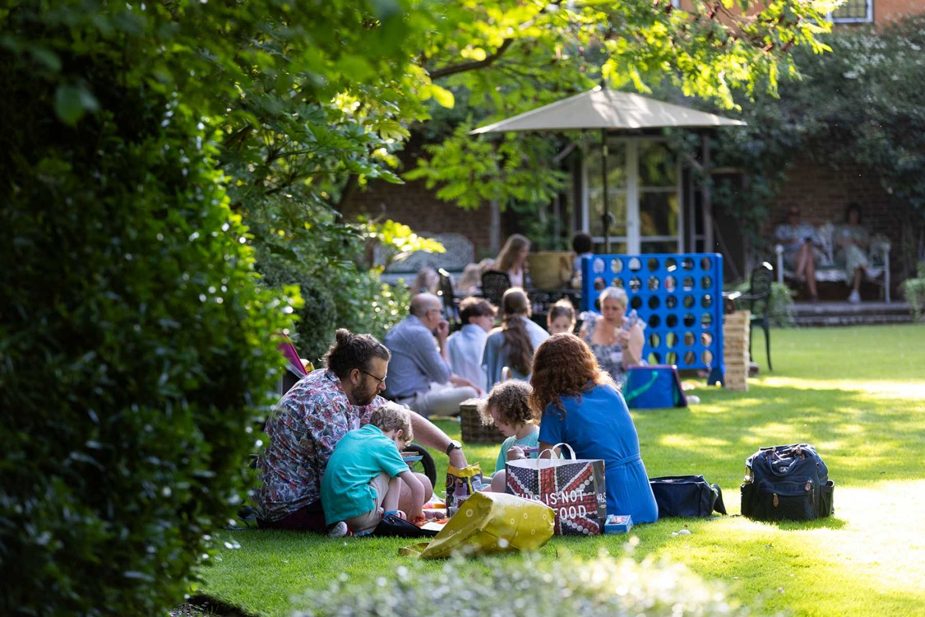 Adults and children sitting out on a lush green lawn in a summer's day having picnics together