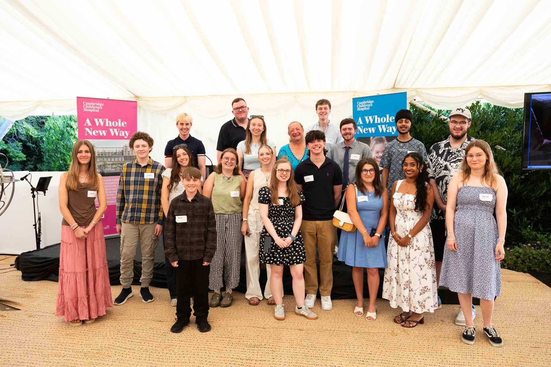 A group of young people standing together with a woman in a turquoise dress who looks very proud of them all